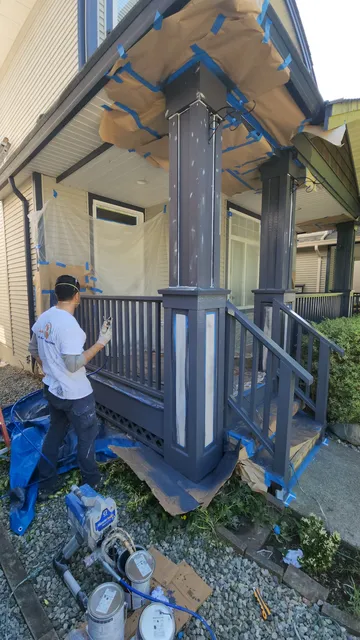 Painter spraying a masked charcoal-blue porch column on a cream-sided home
