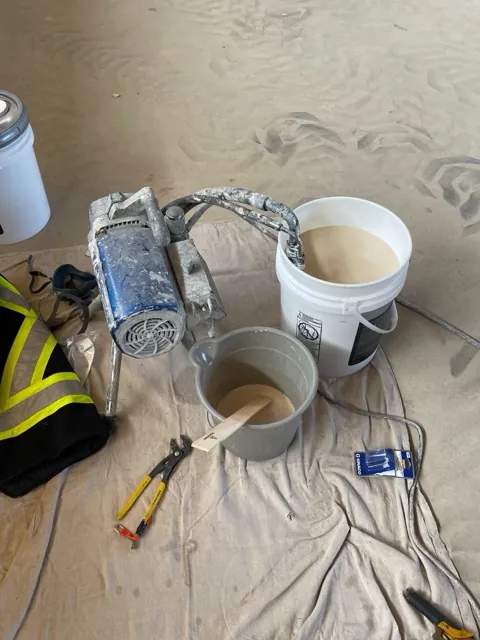 Airless sprayer and pails of clear wood coating mixed out on a drop cloth during a mass timber coating project